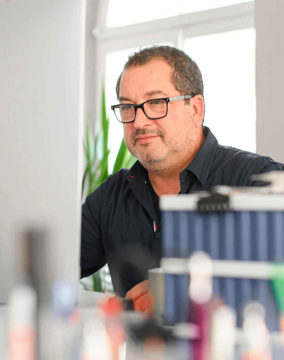 Mann mit Brille sitzt an einem Schreibtisch mit Computer.