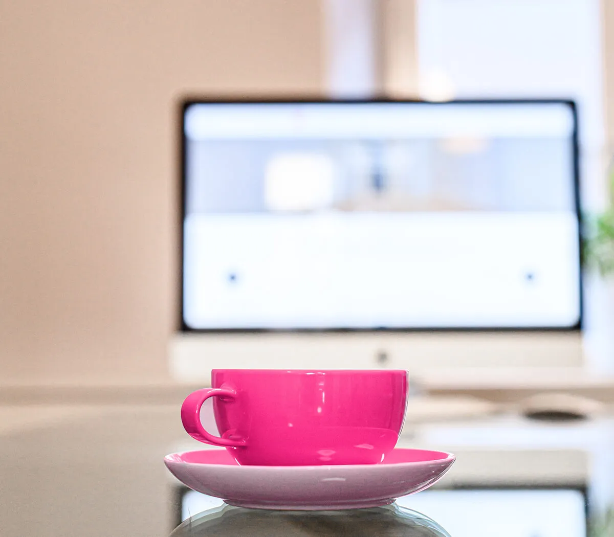 Pinke Tasse auf einem Tisch vor einem Computer.